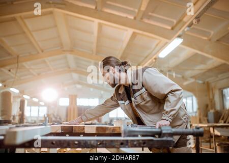 Bel falegname in uniforme incollaggio di barre di legno con pressioni a mano alla produzione di carpenteria Foto Stock