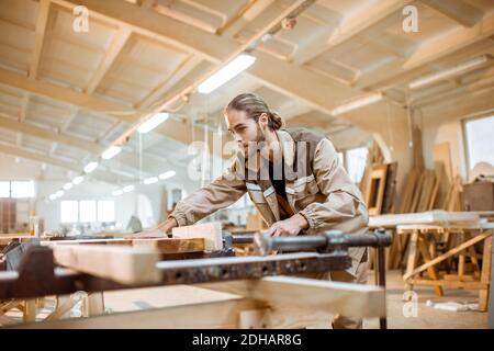 Bel falegname in uniforme incollaggio di barre di legno con pressioni a mano alla produzione di carpenteria Foto Stock