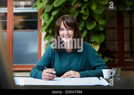 Ritratto di sorridente architetto femminile con disegno al tavolo cortile Foto Stock
