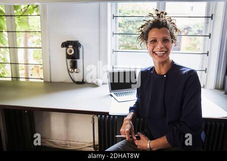 Ritratto di sorridente architetto femminile seduto al tavolo in ufficio Foto Stock