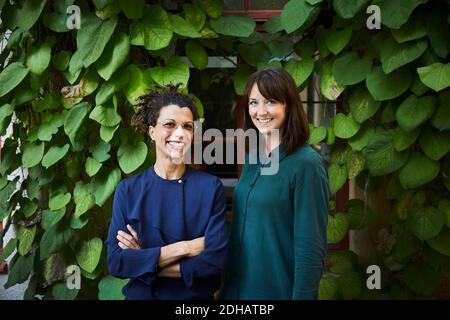 Ritratto di sorridenti architetti femminili in piedi contro le piante superriduttore in cortile Foto Stock