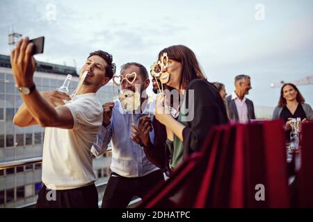 Colleghi aziendali che tengono dei puntelli durante i selfie durante le celebrazioni in ufficio sulla terrazza Foto Stock