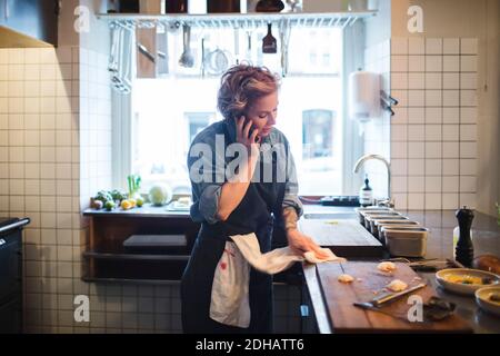 Chef donna che parla sul telefono cellulare durante la pulizia della cucina contatore nel ristorante Foto Stock