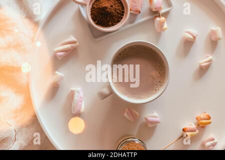 Tazza in ceramica di cioccolato caldo o cacao con marshmallow su tavola bianca. Bevanda da dessert invernale. Stile di posa piatto. Decorazioni ghirlande di luci. Foto Stock