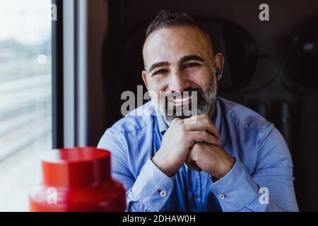 Ritratto di uomo d'affari sorridente con le mani aggrappate seduti in treno Foto Stock