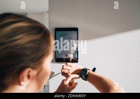 Orologio intelligente da adolescente con tablet digitale montato parete bianca a casa Foto Stock