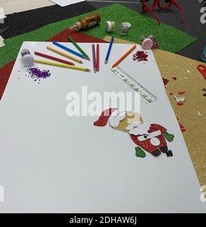 Un'immagine verticale di Babbo Natale, matite colorate e glitter sparsi su carte di colori diversi con spazio di copia Foto Stock