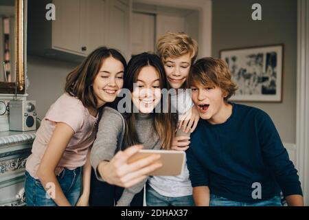 Amici allegri che prendono selfie attraverso lo smartphone mentre si è in piedi casa Foto Stock