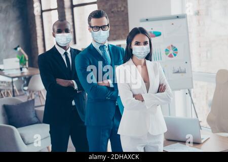 Elegante e moderno business trio squali in tux con braccia ripiegate maschere di sicurezza a garza per la prevenzione del cov nella postazione di lavoro Foto Stock