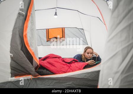 Ragazza adolescente che usa lo smartphone mentre si sdraiava in tenda Foto Stock