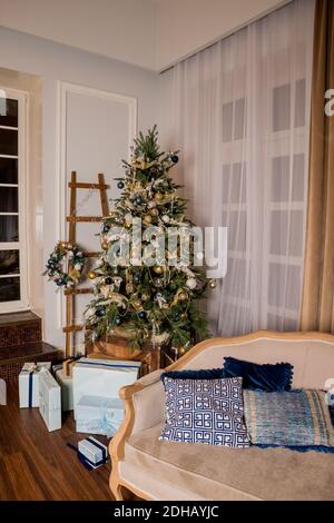 Elegante camera con un grande Natale di abete blu innevato, decorata con una ghirlanda, palline dorate Foto Stock