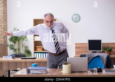 Anziano dipendente di sesso maschile che soffre di radiculite sul posto di lavoro Foto Stock