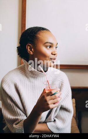 Sorridente ragazza adolescente che guarda via mentre ha frullato a casa Foto Stock