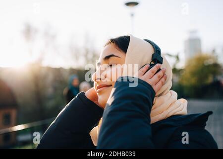 Ragazza adolescente che ascolta le cuffie con gli occhi chiusi contro il cielo Foto Stock