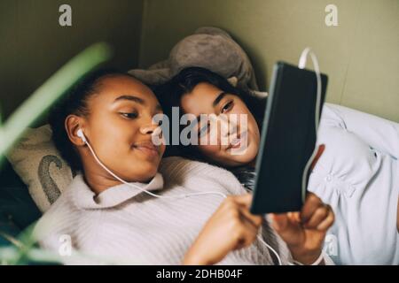 Adolescenti che ascoltano musica su un tablet digitale mentre si sdraiano letto a casa Foto Stock