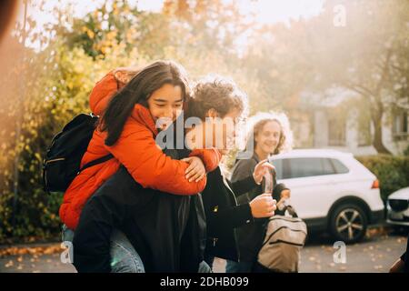 Adolescente ragazzo piggybacking femmina mentre si parla con gli amici in città Foto Stock