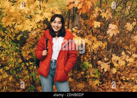 Ritratto di sorridente adolescente in piedi con zaino contro l'autunno alberi Foto Stock