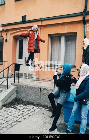 Donna con amici che fotografano l'equilibrio femminile sulla ringhiera contro l'edificio in città Foto Stock