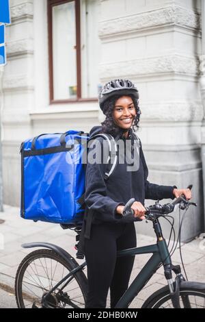 Ritratto di sorridente donna con consegna in bicicletta in città Foto Stock