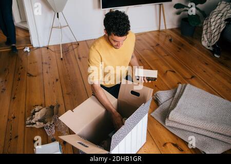 Vista ad angolo alto dell'uomo che rimuove i romanzi dalla scatola di cartone a casa nuova Foto Stock