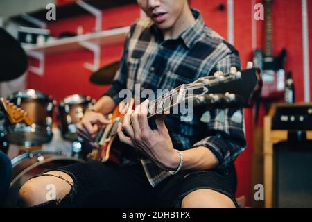 Sezione centrale dell'uomo che suona la chitarra mentre si siede nello studio di registrazione Foto Stock