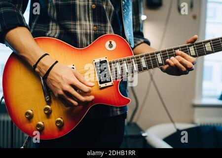 Sezione centrale dell'uomo che suona la chitarra mentre si prova in studio di registrazione Foto Stock