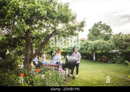 Amici maschili e femminili che preparano il cibo sul barbecue mentre la famiglia divertirsi in cortile Foto Stock