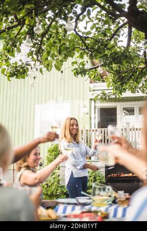 Donna matura che prepara il cibo sul barbecue mentre tostando gli occhiali da vino con amici al party sul cortile Foto Stock