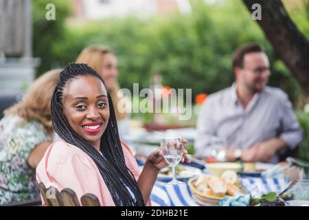 Ritratto di donna sorridente che ha vino mentre si siede con gli amici a festa in giardino Foto Stock