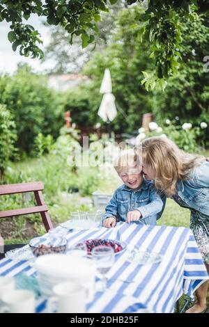 Felice madre baciando suo figlio al tavolo da pranzo in cortile Foto Stock