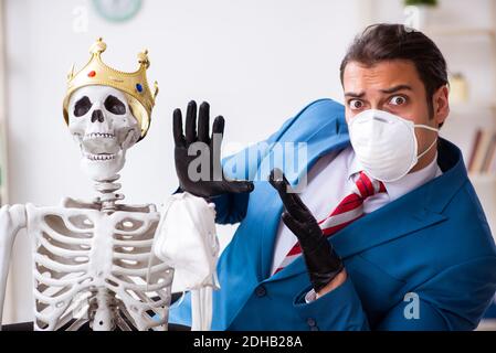 Giovane uomo d'affari e scheletro in ufficio in concetto pandemico Foto Stock