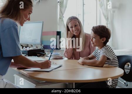 Madre e figlio che consultano la pediatra femminile alla scrivania in clinica Foto Stock