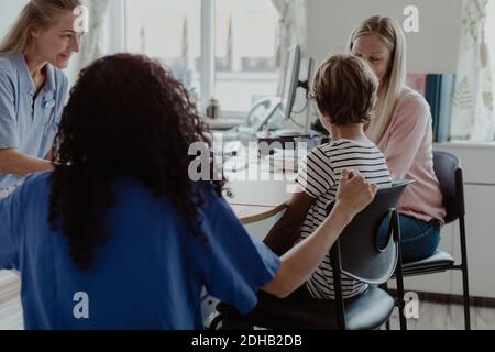 Madre e figlio che consultano il medico mentre l'infermiera femminile si siede vicino scrivania in clinica Foto Stock