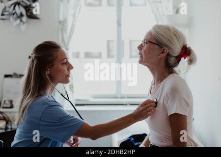 Vista laterale del medico di sesso femminile che esamina la paziente anziana in medicina clinica Foto Stock