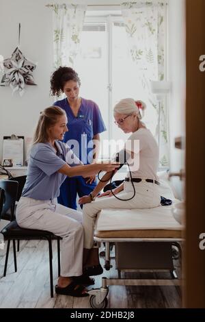 Donna matura dottore che controlla la pressione sanguigna della donna anziana in clinica Foto Stock