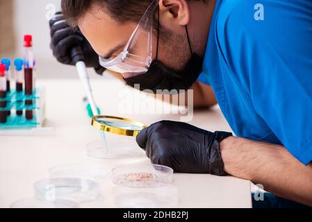 Giovane biochemista maschile che esamina campioni di sangue in concetto pandemico Foto Stock