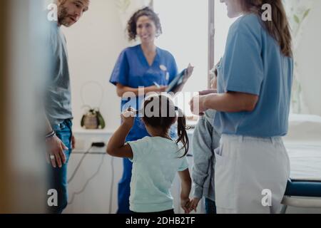 Padre che parla con i bambini mentre gli operatori sanitari li guardano in sala di visita medica Foto Stock