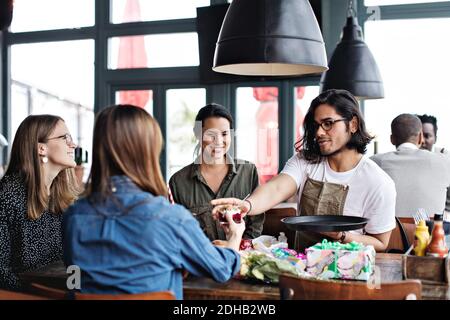 Cameriera che serve bevande alle giovani amiche sorridenti che si siedono tavolo da pranzo nel ristorante Foto Stock