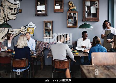 Il proprietario parla con amici multietnici mentre la famiglia ha il brunch a. tavolo nel ristorante Foto Stock