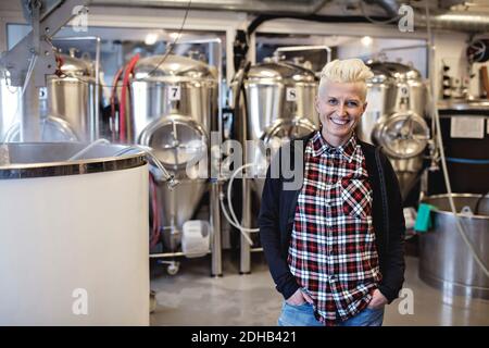 Ritratto di sorridente manager femminile in piedi con le mani in tasca presso la fabbrica di birra Foto Stock