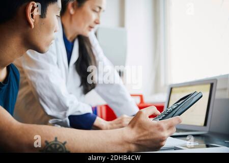 Giovane studente di ingegneria maschile che tiene calcolatrice da insegnante maturo in in aula Foto Stock