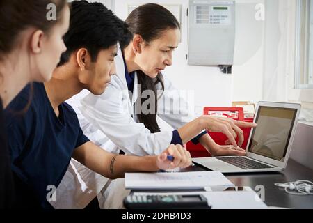 Insegnante che indica lo schermo del laptop ai giovani studenti di ingegneria in aula Foto Stock
