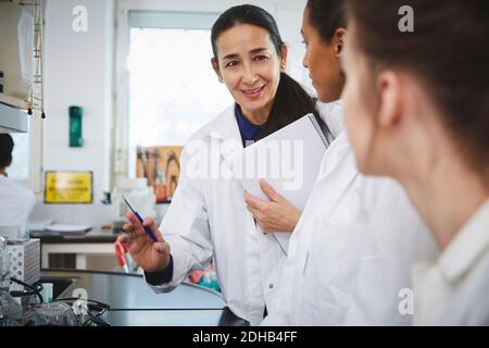 Insegnante maturo sicuro che spiega alle giovani studentesse universitarie dentro laboratorio chimico Foto Stock
