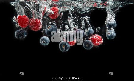 Mirtilli e lamponi che spruzzano nell'acqua cristallina con aria bolle e affondamento Foto Stock