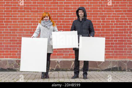 Giovane uomo e donna in piedi su uno sfondo di a. muro di mattoni rossi che contiene tre tele bianche di fronte per dipingere Foto Stock