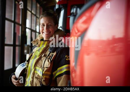 Ritratto di sorridente pompiere femminile in piedi da motore di fuoco a. stazione dei vigili del fuoco Foto Stock