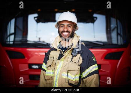 Ritratto di pompiere sorridente in piedi davanti al motore antincendio alla stazione dei vigili del fuoco Foto Stock