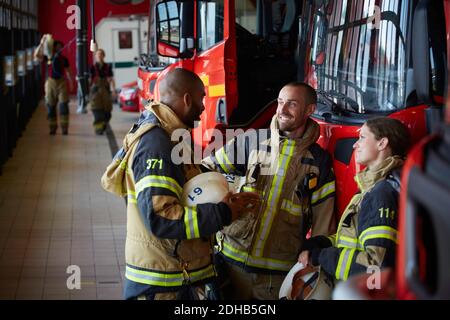 Vigili del fuoco in uniforme che parlano mentre si è in piedi alla stazione dei vigili del fuoco Foto Stock