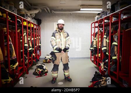 Lunghezza completa del pompiere maschile in piedi in spogliatoio a. stazione dei vigili del fuoco Foto Stock