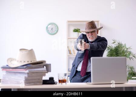 Divertente vecchio capo in cappellino cowboy in ufficio Foto Stock